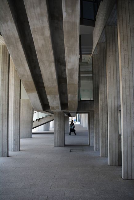 A person walking under a modern concrete structure with geometric columns and stairs.