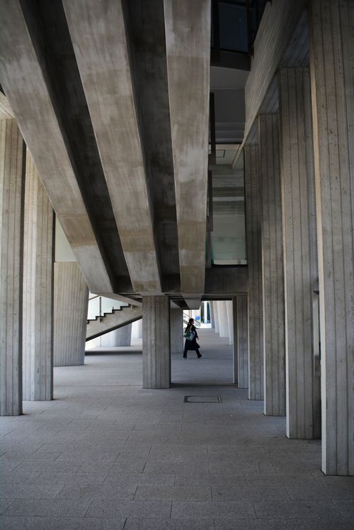 Free A person walking under a modern concrete structure with geometric columns and stairs. Stock Photo