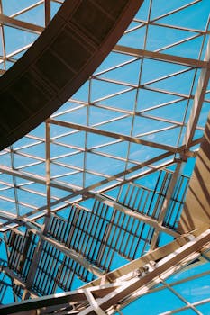 在清澈的蓝天下，现代玻璃天花板以动态视角展示几何图案