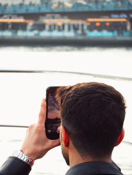 A man capturing a scenic river view with his smartphone, perfect for travel and technology themes.