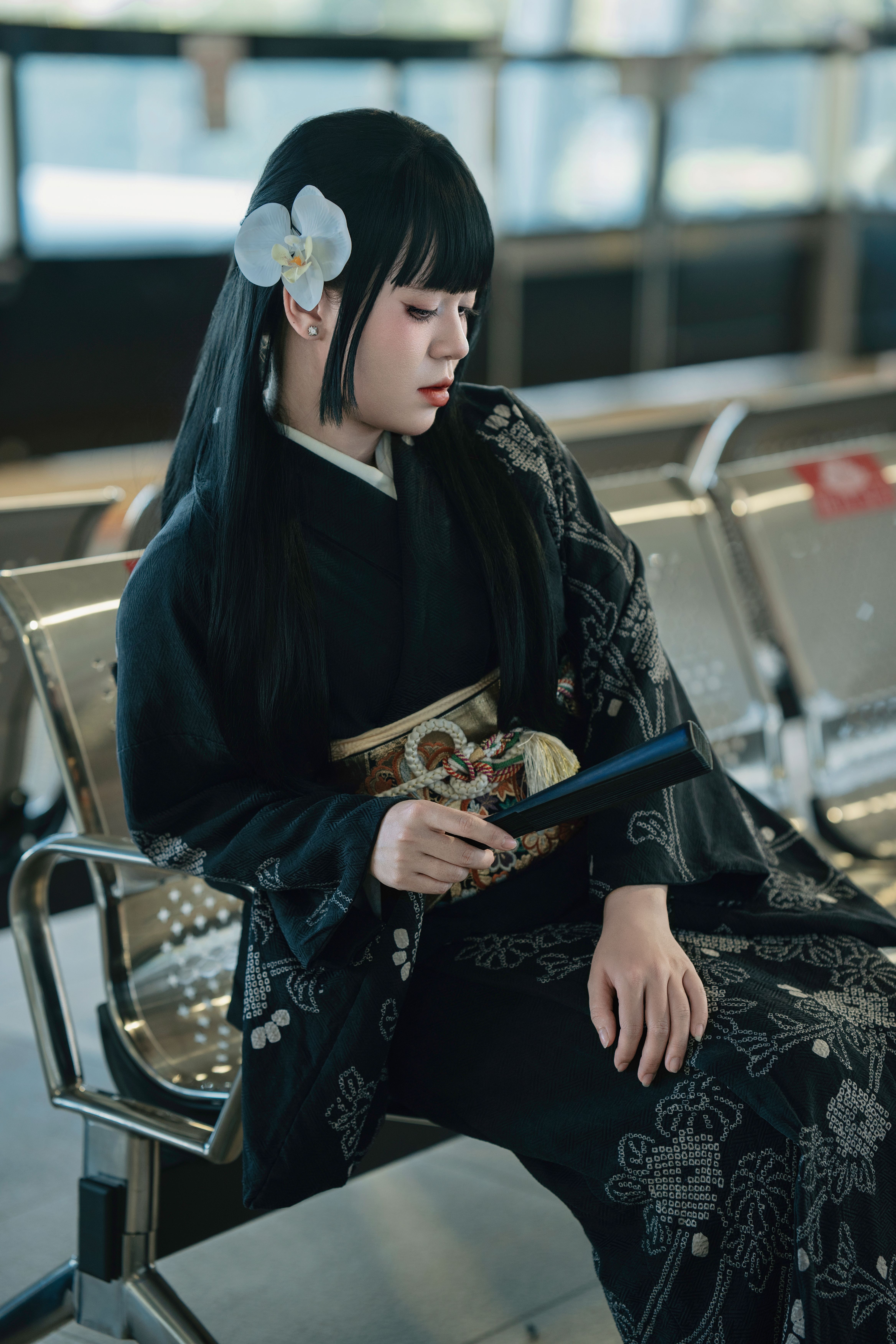 A woman in a black kimono with orchid accessory seated indoors.