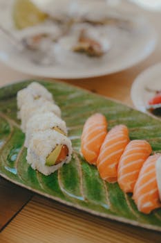 A vibrant sushi platter featuring sushi rolls and salmon nigiri on a green leaf plate.