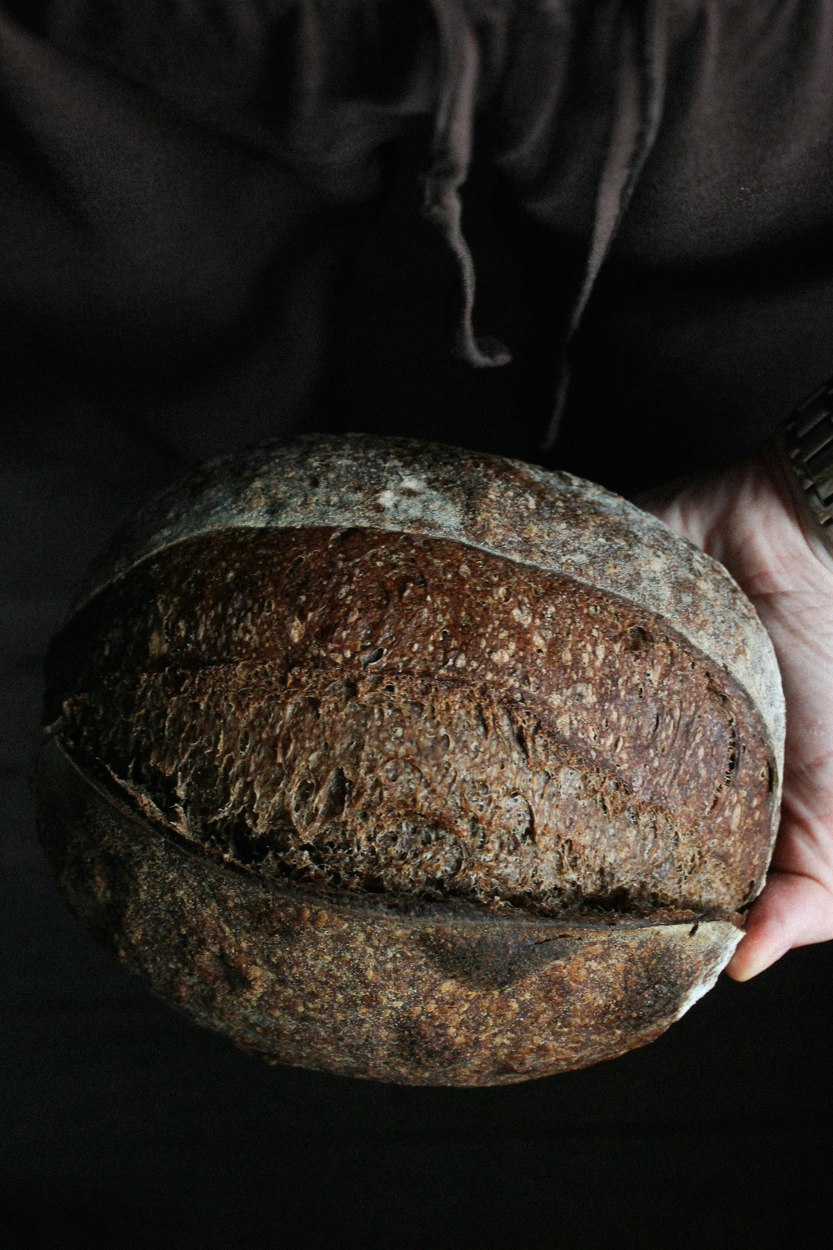 Close-up of a hand holding a crusty, rustic loaf of artisan bread.