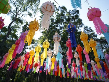 Colorful paper lanterns hanging outdoors at a festival in Thailand under a clear day sky.