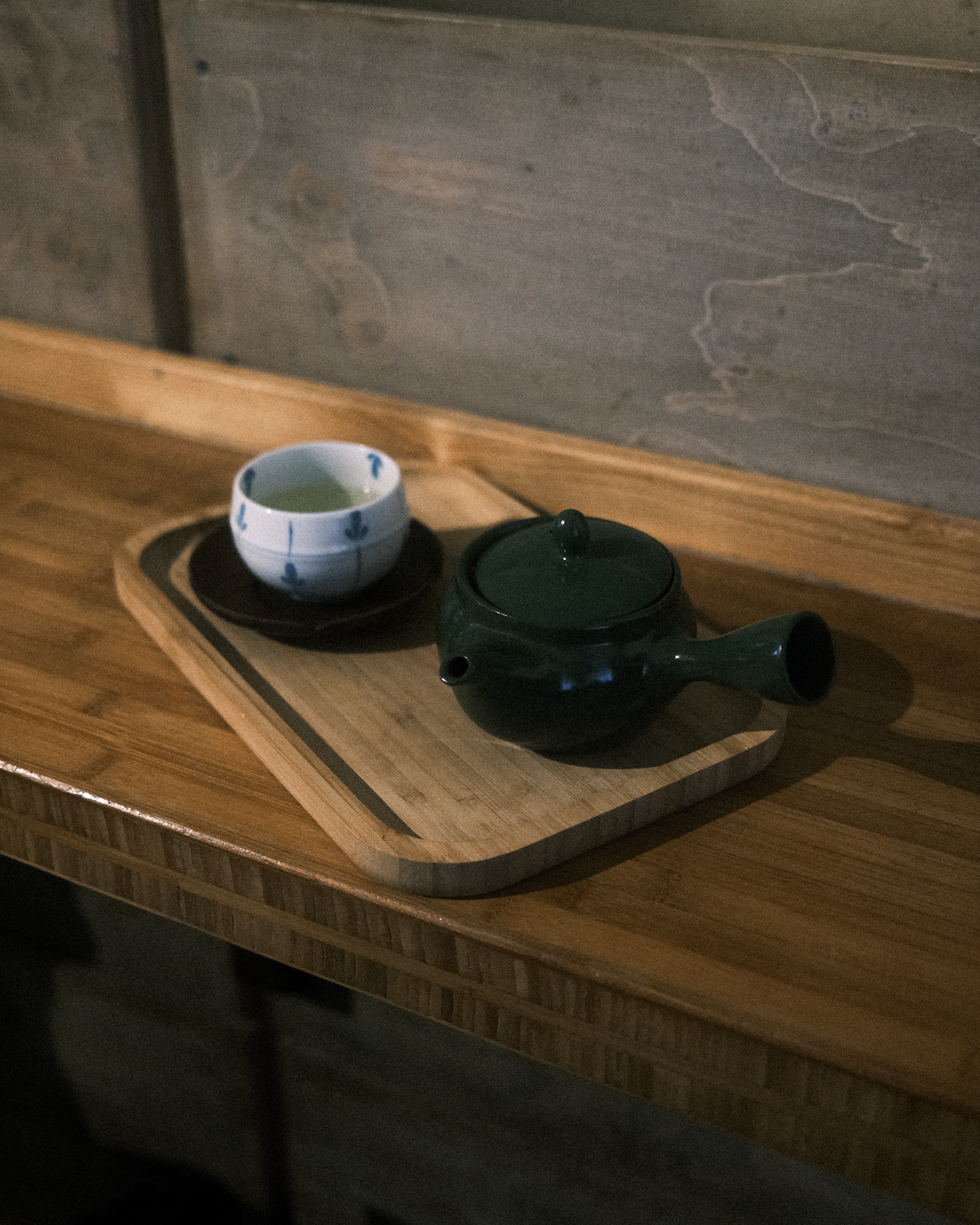 A Japanese teapot with a cup on a wooden tray, set in a warm indoor atmosphere.