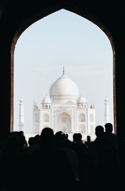 A large crowd views the iconic Taj Mahal in Agra, silhouetted against the bright sky.
