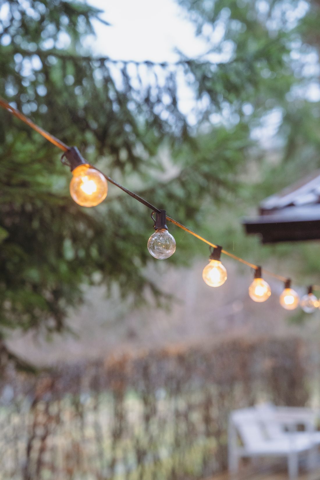 Warm festoon lighting over a landscaped garden seating area at dusk