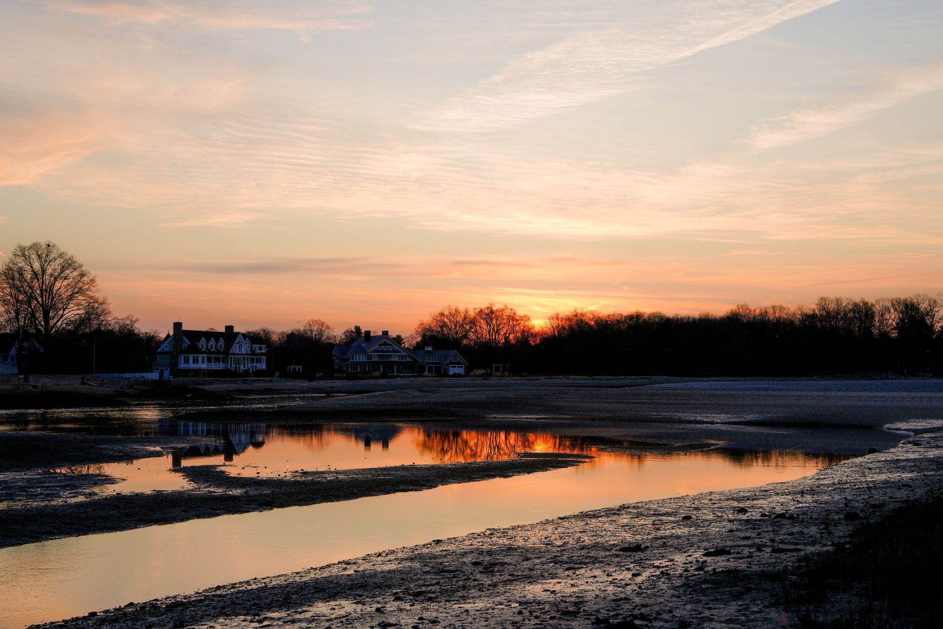 A tranquil sunrise over Cove Island Park in Stamford, Connecticut, reflecting on a calm inlet with silhouetted trees and houses.