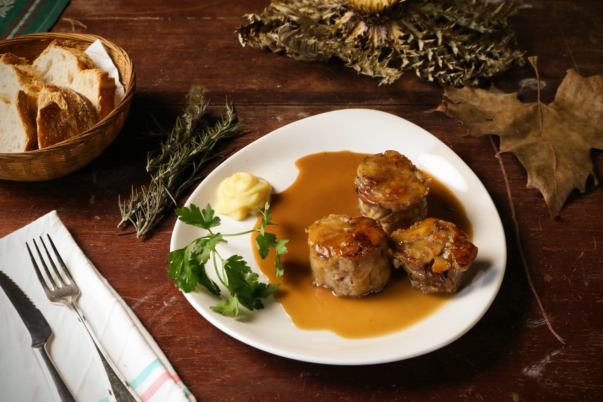 Farfurie cu carne în sos și pâine, pe o masă rustică de lemn