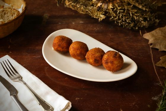 Four golden round arancini on an oval white plate with cutlery on a wooden table