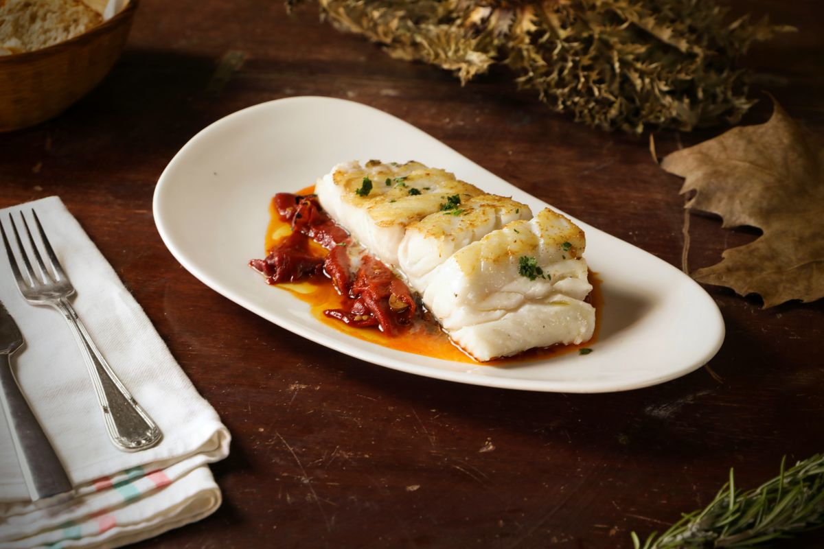 Roasted cod loin with golden top and parsley on red piquillo pepper sauce, oval white plate