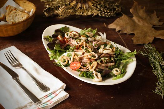 A vibrant seafood salad with fresh cherry tomatoes and greens on a rustic table setting.