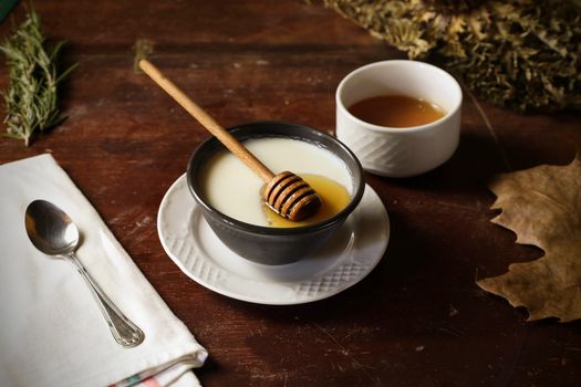 A rustic still life with honey, tea, and autumn leaves on wooden table.