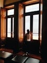 一名妇女站在高高的木制门边，凝视着门外，自然光洒满了房间