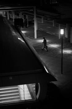 Black and white photo of a lone man walking at night in a Japanese urban setting.