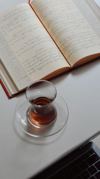 Open notebook with handwriting beside a glass of tea and laptop on a desk, ideal for study or work themes.