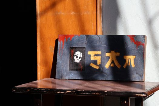A vintage sign featuring a skull and abstract letters, showcased on a rustic wooden table in a sunlit room.