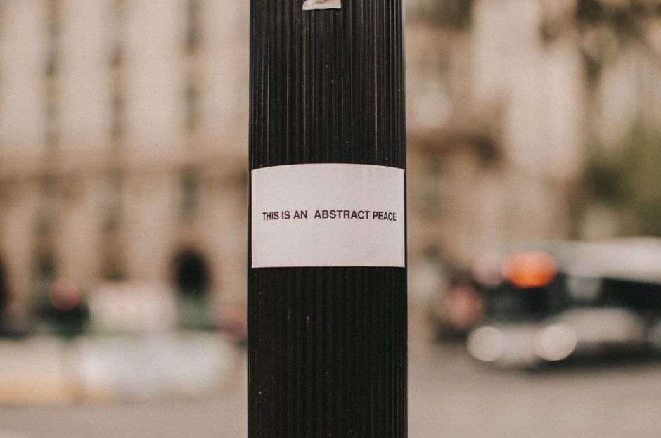 Close-up of a street pole with an 'abstract peace' message, in an urban setting with a blurry backdrop.