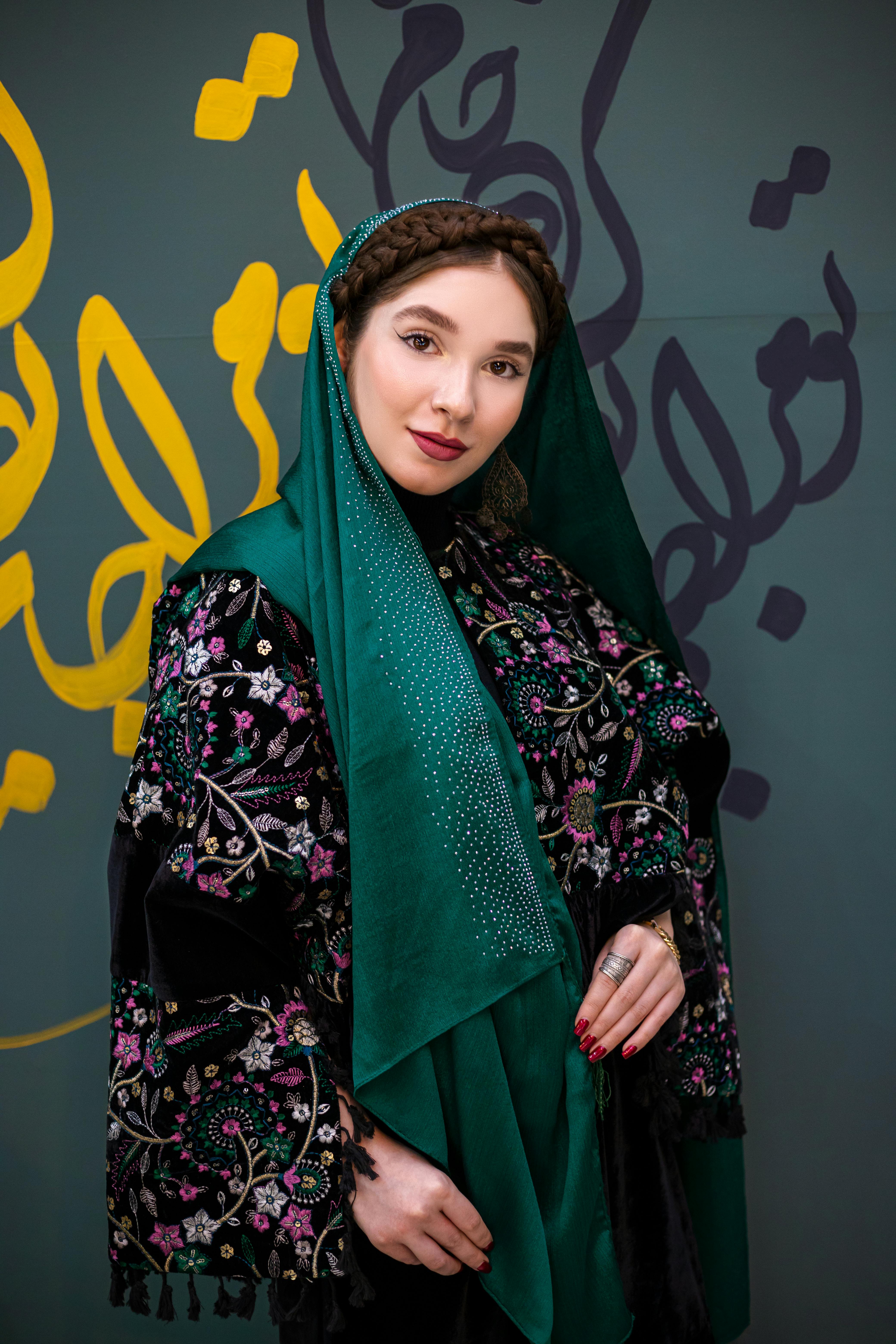 Woman in traditional clothing with intricate embroidery stands before an artistic backdrop.