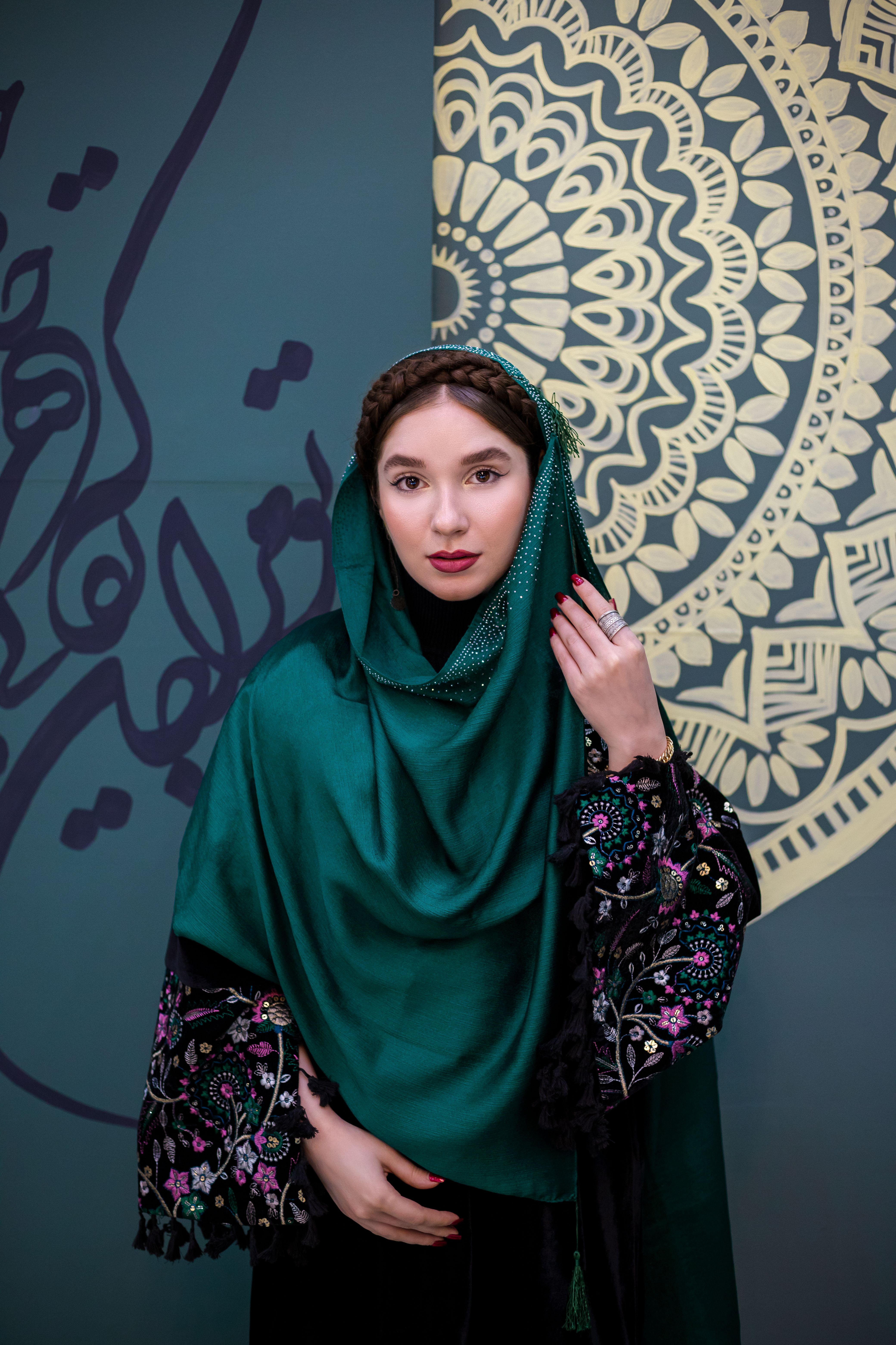 Elegant woman in a green shawl against ornate patterned background.
