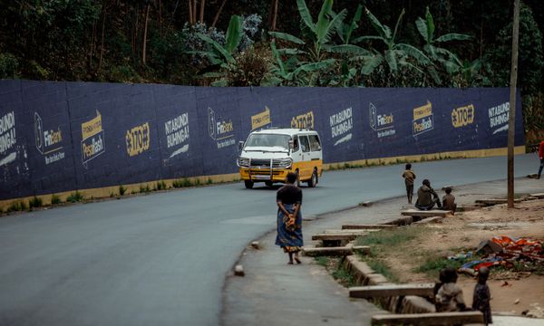 After-School Transport (Scholar Transport) — Minibus driving along a street lined with colorful advertisements and tropical foliage.