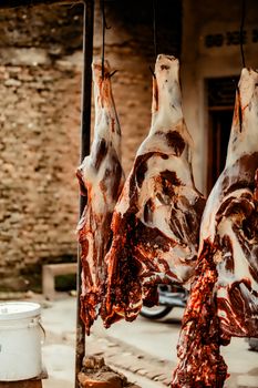 Rustic setting with raw meat hanging, showcasing traditional butchery methods outdoors.