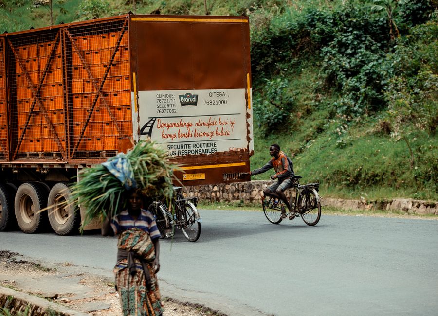 Rural African street scene with cyclists and a large truck in a lush green setting.