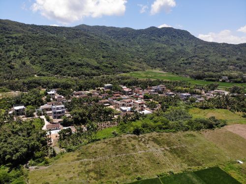 Free A scenic aerial view of a small village surrounded by lush green hills under a blue sky. Stock Photo