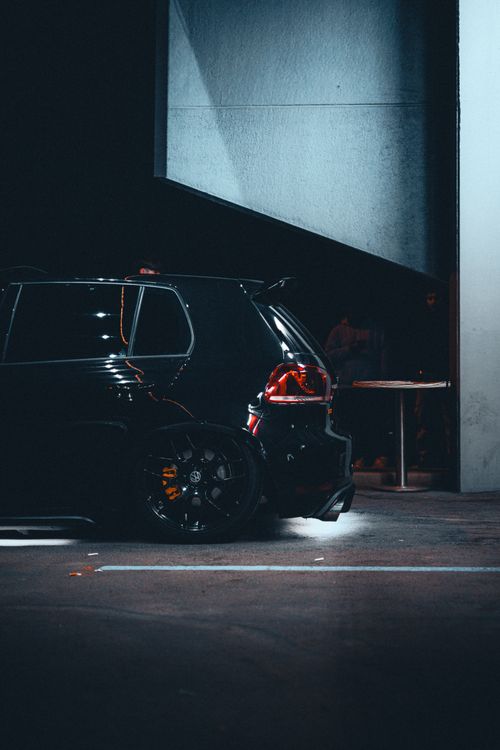 Free Sleek black car parked at night under modern architecture with dramatic lighting. Stock Photo