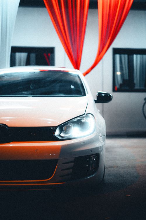 Free White car illuminated under vibrant red drapes in a dimly lit garage, exuding mystery. Stock Photo