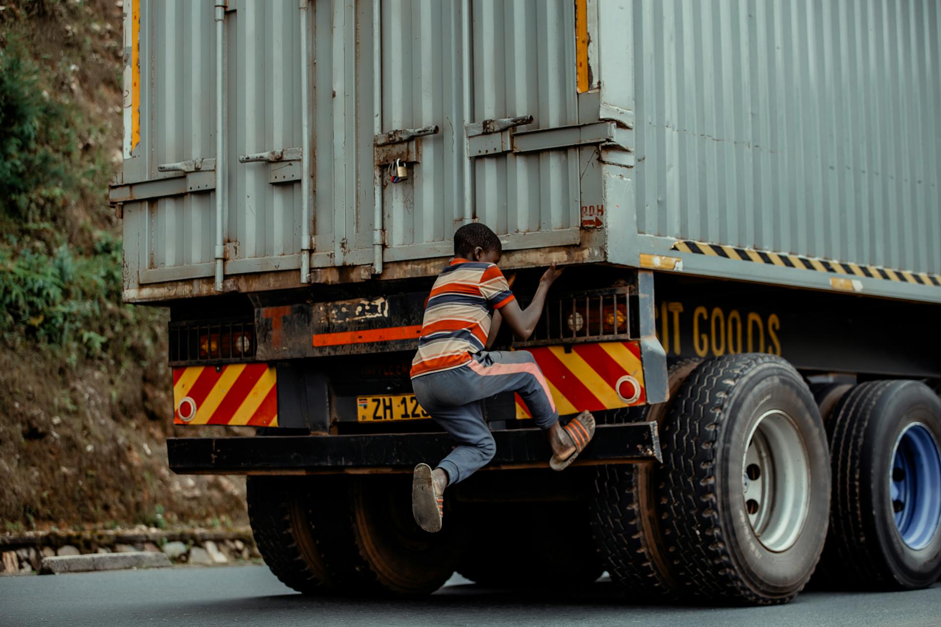 A young child in striped clothing climbs a parked freight truck outdoors, showcasing adventure and curiosity.