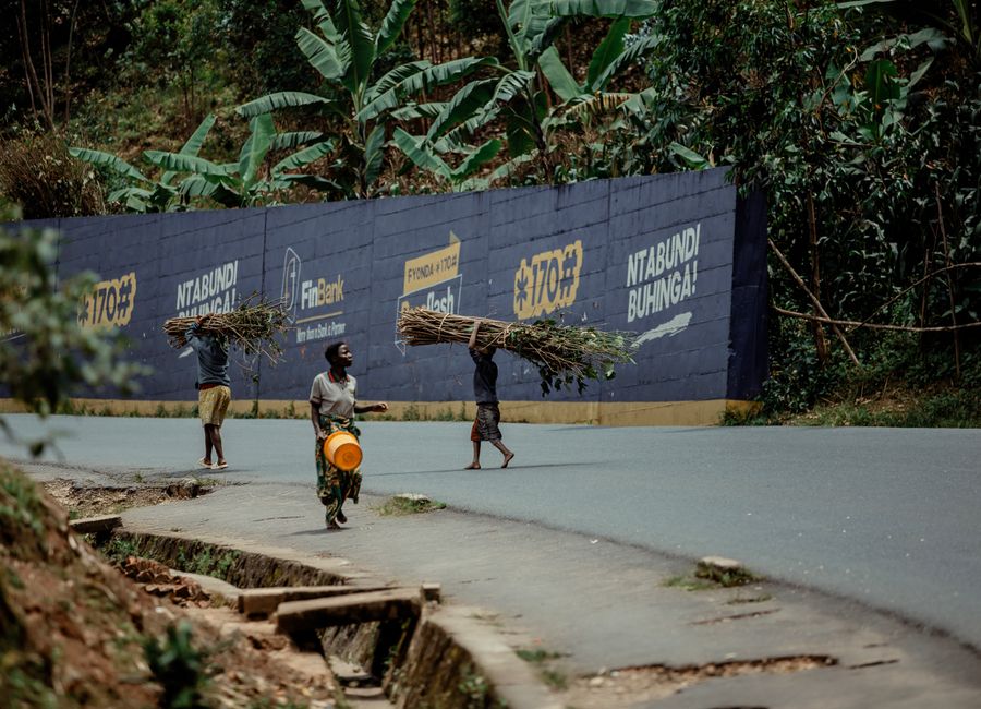 Three individuals walking along a road carrying firewood atop their heads.