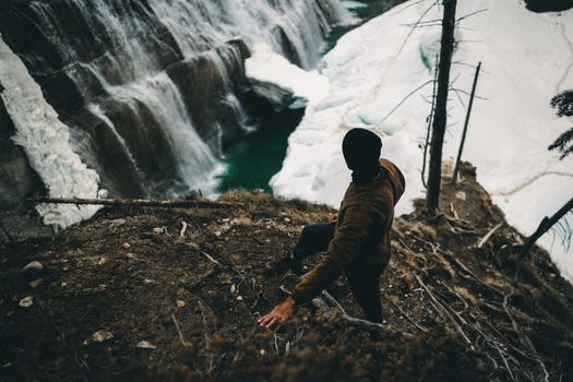 A hiker stands on a cliff above a scenic frozen waterfall in Field, British Columbia, Canada.