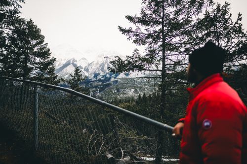 Free A hiker in a red jacket admires the Canadian Rockies from a forest viewpoint. Stock Photo