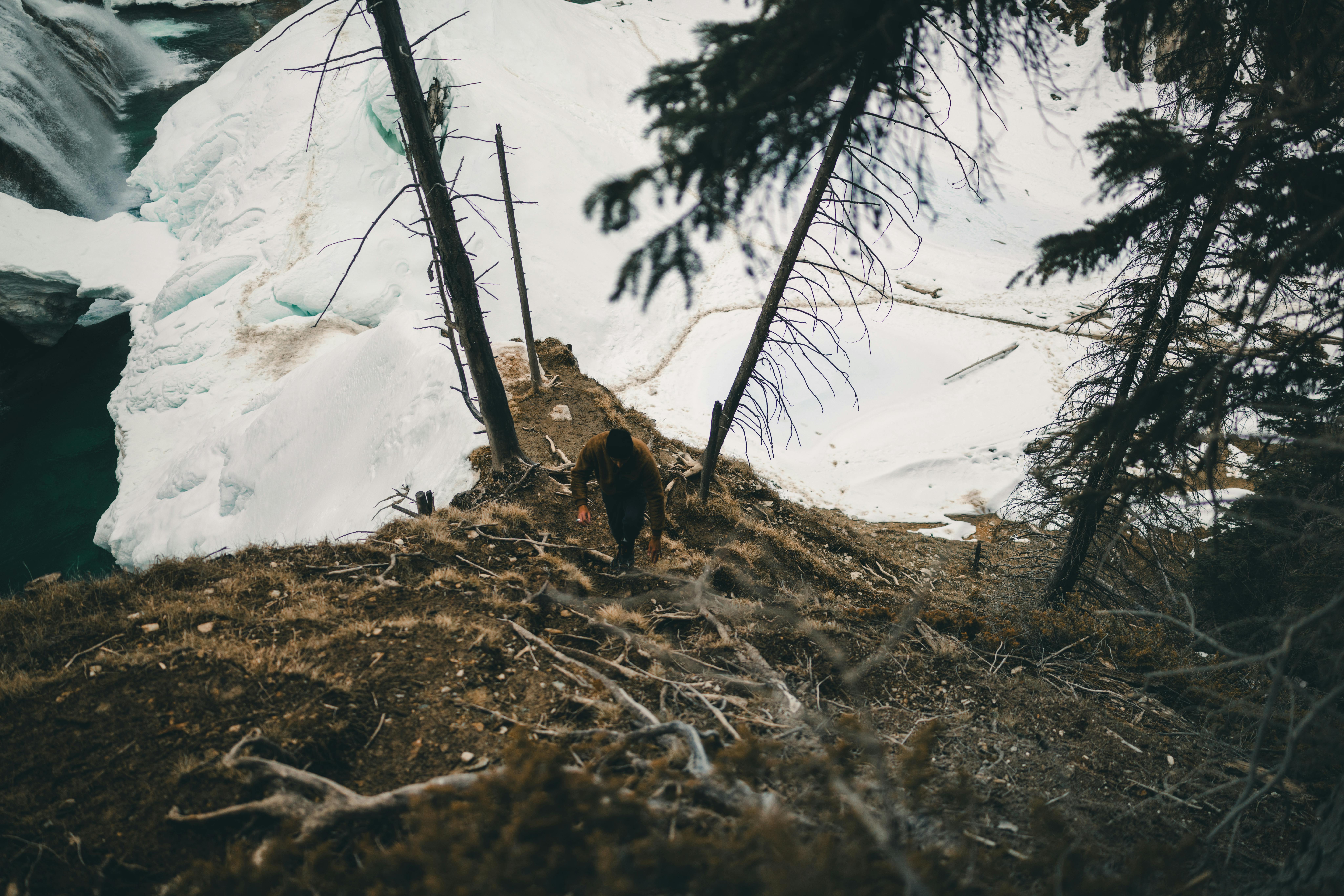 Adventurous hiker climbing steep path in snowy forest near waterfall in Field, British Columbia.