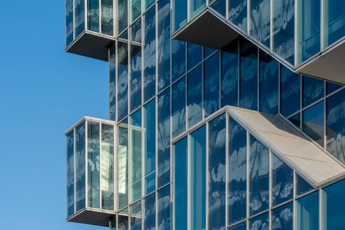 Free Abstract view of a modern building facade with glass reflections against a clear blue sky. Stock Photo