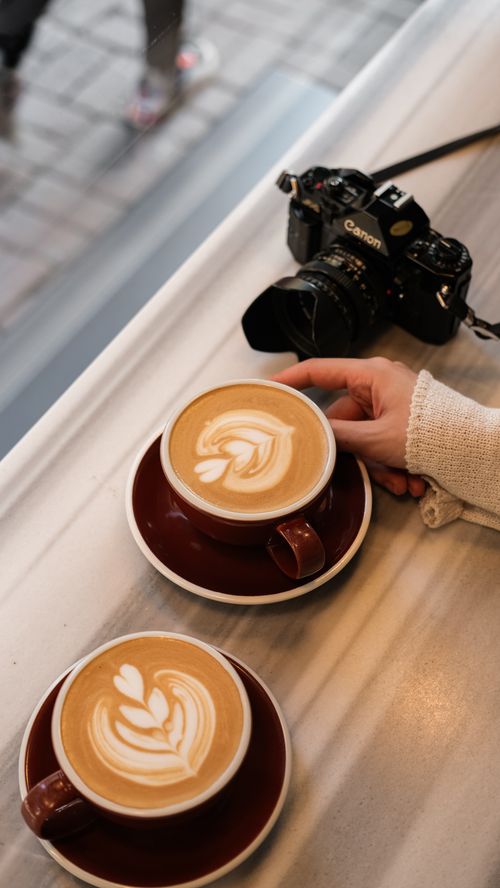Free Two cappuccinos with latte art and a camera on a cafe table. Stock Photo