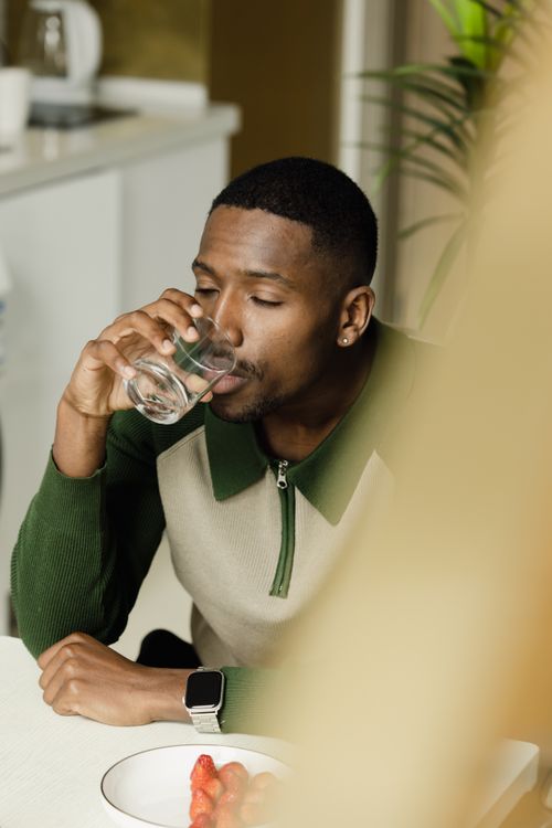 Free A man enjoying a glass of water at a table with strawberries. Stock Photo