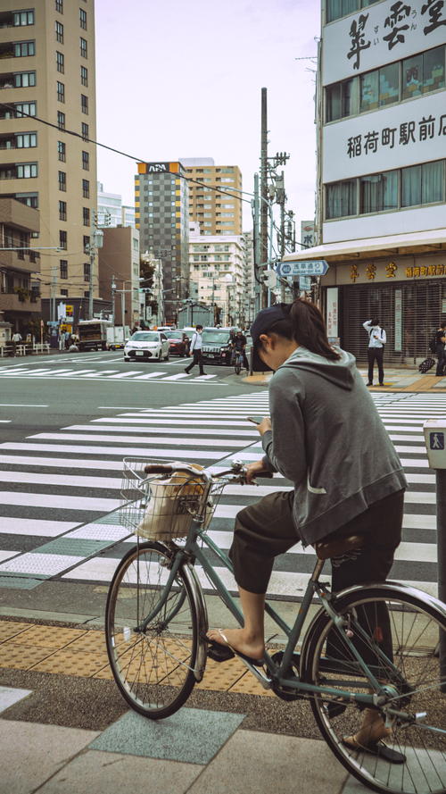 Free A street scene in central Tokyo featuring a casual cyclist waiting at a crosswalk with urban buildings in the background. Stock Photo