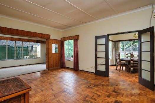 An empty open floor living and dining room with wooden flooring and large windows.