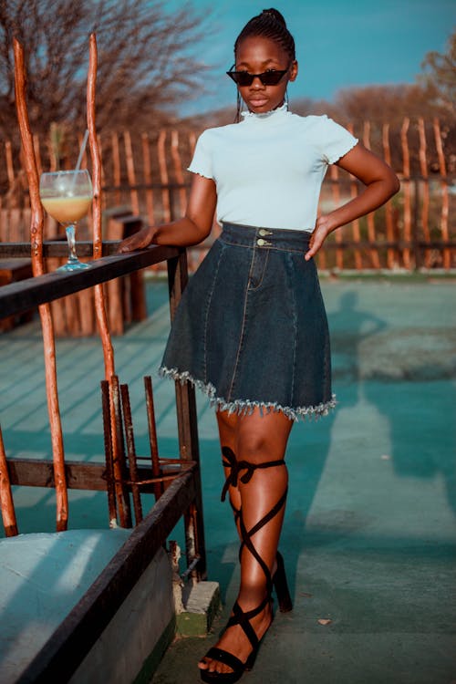 Selective Focus Photo of Standing Woman in White Shirt and Blue Denim Skirt Posing by Wooden Railing