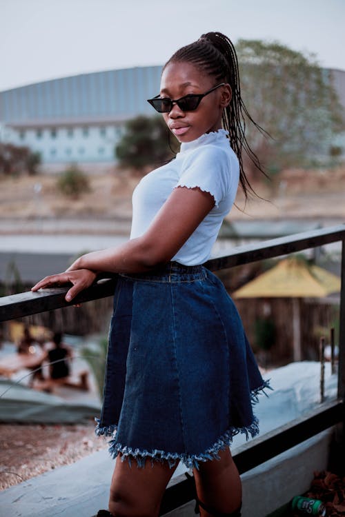 Selective Focus Photo of Woman in White Top and Blue Denim Skirt Posing by Wooden Railing