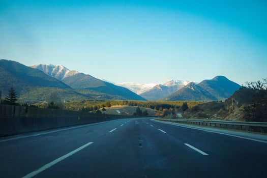 A clear highway leading through a picturesque mountain range under a bright blue sky.