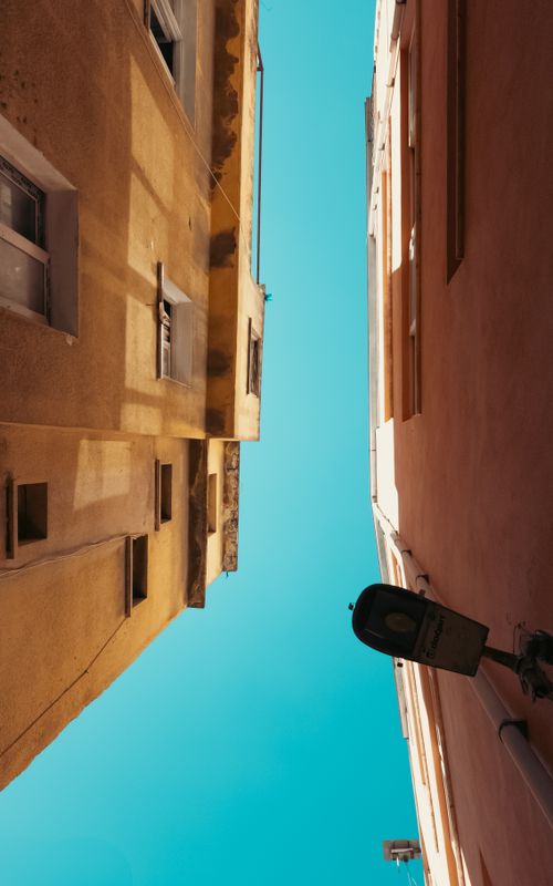 Free Looking up at narrow alleyway between pastel buildings against a clean blue sky. Stock Photo