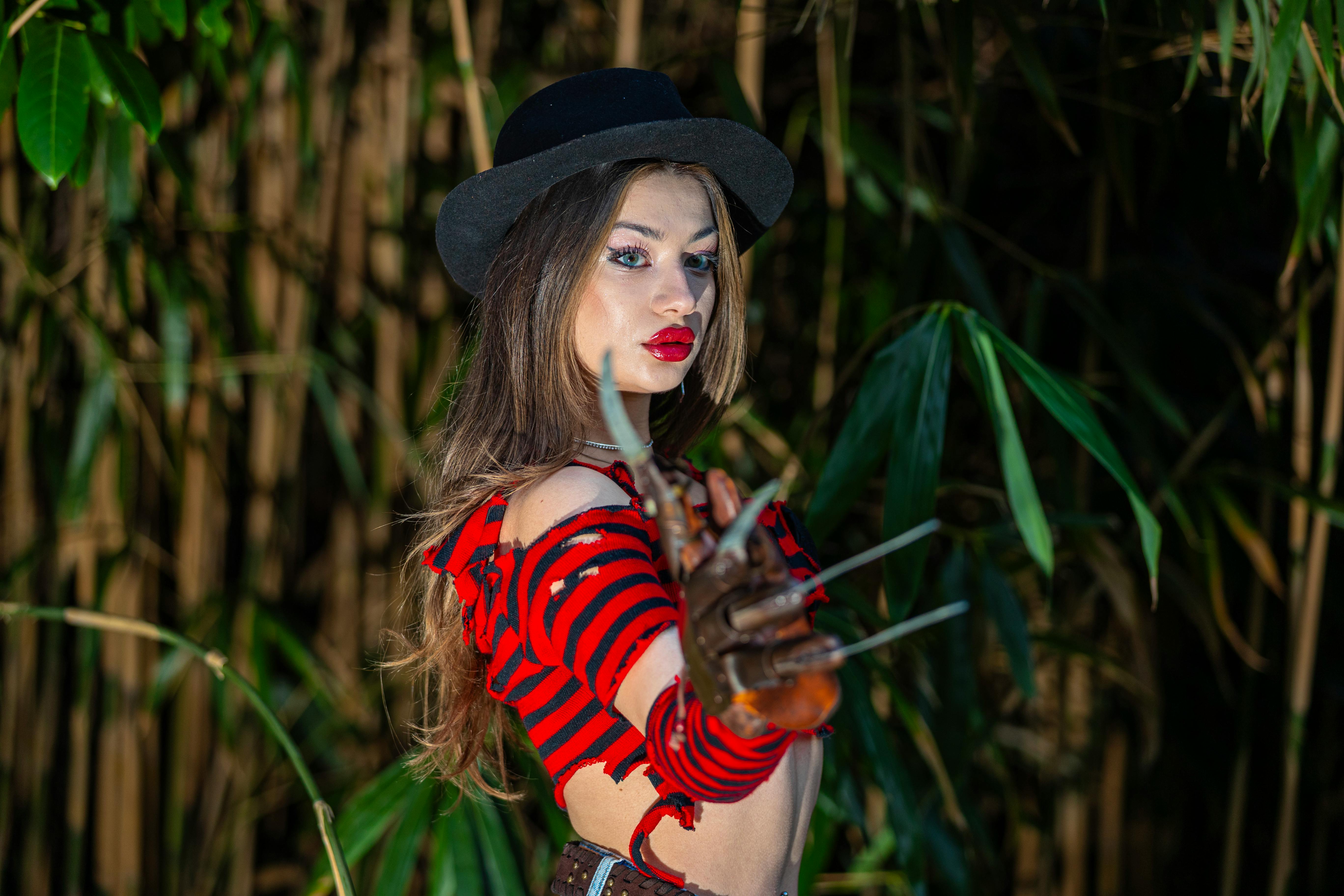 A woman in a red and black striped costume with a claw glove poses outdoors.