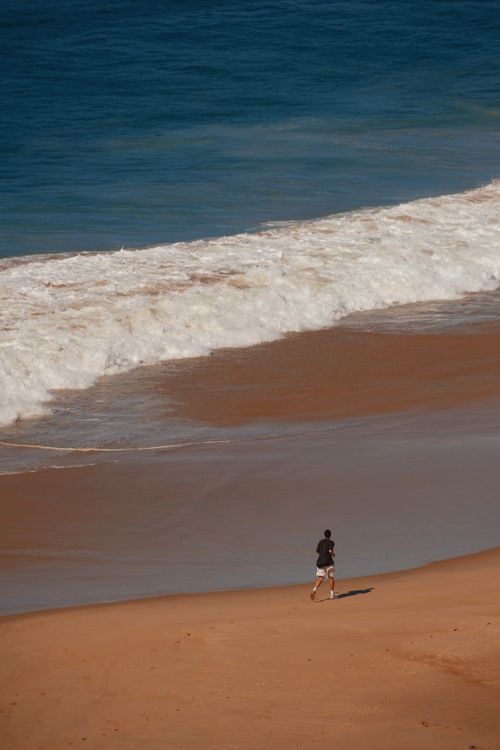 Free A person running along a sandy beach with ocean waves in the background on a sunny day. Stock Photo