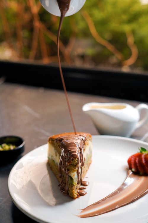 Free Close-up of a cheesecake slice drizzled with chocolate syrup, served with fresh strawberries. Stock Photo