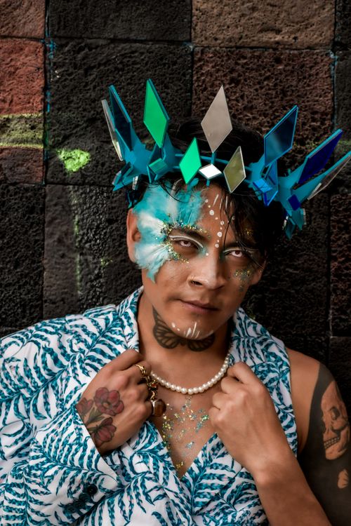 Free Man with artistic makeup and crown, striking pose against textured wall. Stock Photo