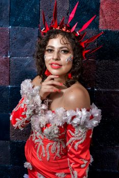 Creative portrait of a woman in a red costume with artistic makeup and headpiece.