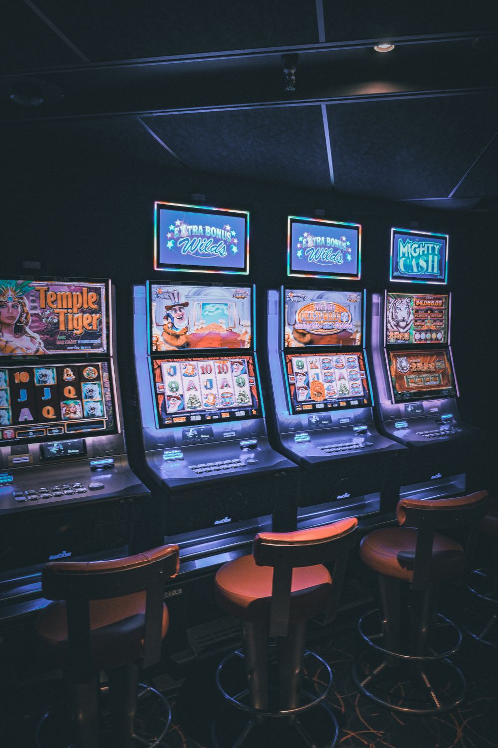 Row of illuminated slot machines in a dimly lit, empty casino area